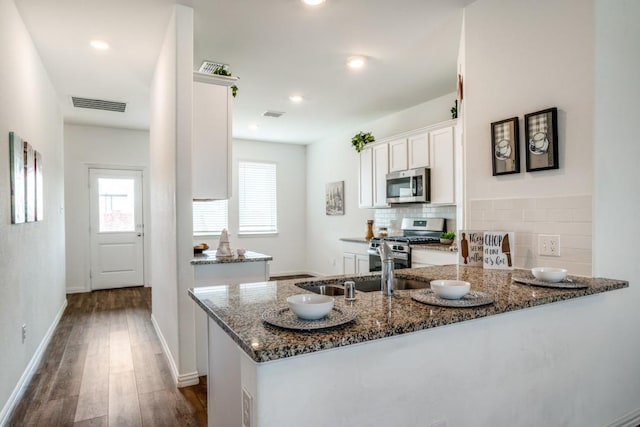 kitchen with backsplash, stainless steel appliances, dark stone counters, and white cabinets