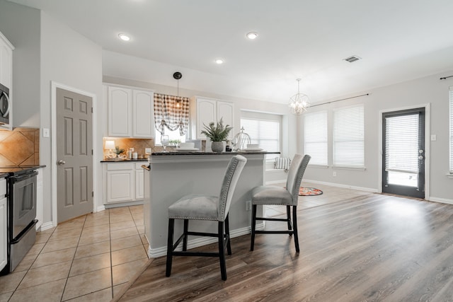 kitchen featuring white cabinetry, decorative light fixtures, a center island, a kitchen breakfast bar, and stainless steel appliances