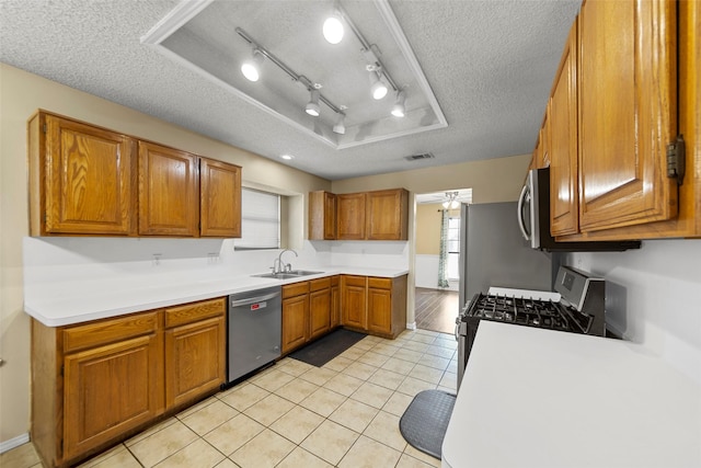 kitchen featuring light tile patterned flooring, sink, a tray ceiling, stainless steel appliances, and a textured ceiling