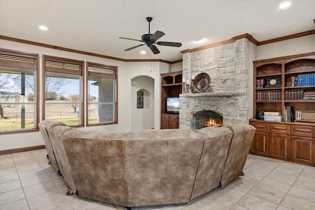 tiled living room featuring crown molding, ceiling fan, and a stone fireplace