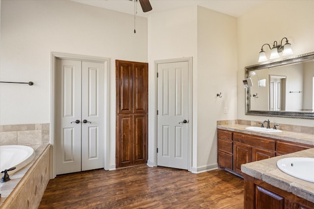 bathroom featuring ceiling fan, vanity, wood-type flooring, and tiled tub