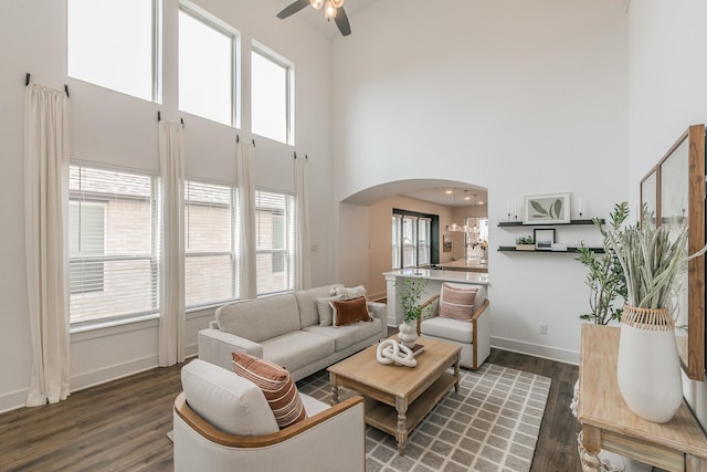 living room with dark wood-type flooring, ceiling fan, and a high ceiling