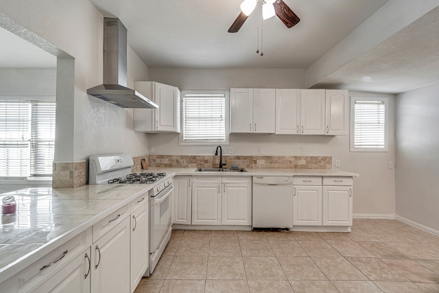 kitchen featuring sink, white cabinets, light tile patterned floors, wall chimney range hood, and white appliances