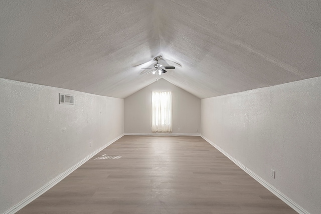 additional living space featuring hardwood / wood-style flooring, vaulted ceiling, and a textured ceiling