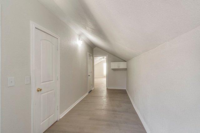 hall featuring lofted ceiling, a textured ceiling, and light wood-type flooring