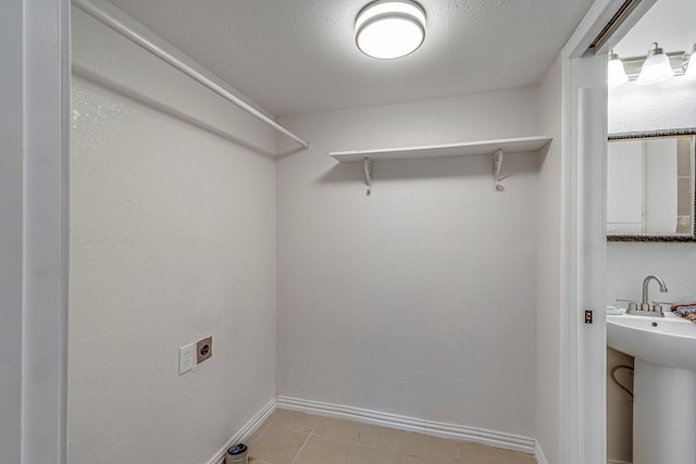 clothes washing area with light tile patterned floors, sink, hookup for an electric dryer, and a textured ceiling