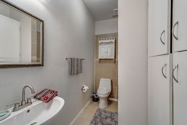 bathroom with tile patterned floors, toilet, sink, and tile walls