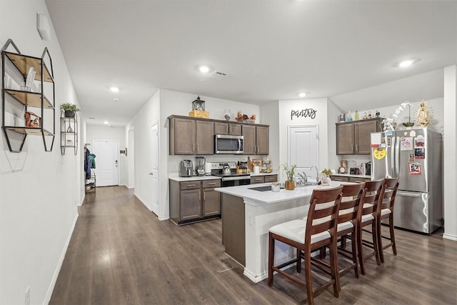 kitchen featuring a breakfast bar area, stainless steel appliances, dark hardwood / wood-style floors, and a center island with sink