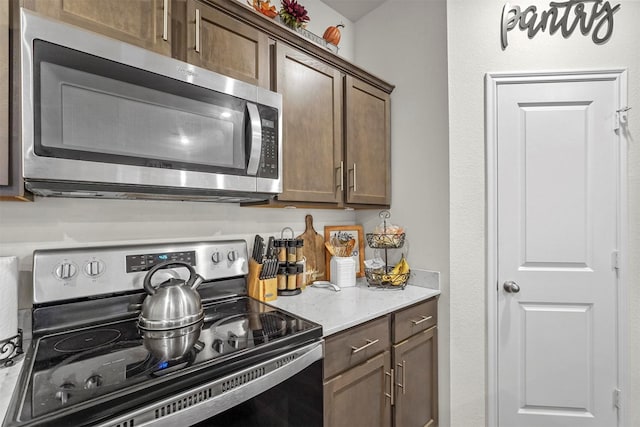 kitchen with stainless steel appliances, light stone countertops, and dark brown cabinets