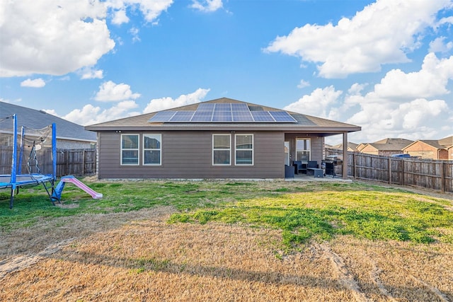 back of house with a patio, a yard, a trampoline, and solar panels