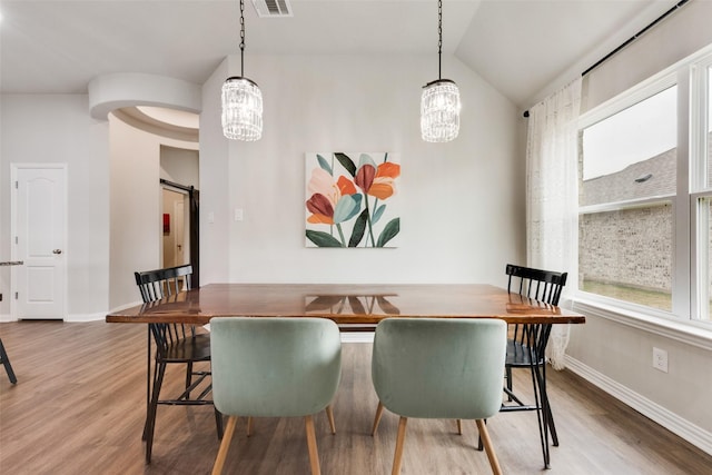 dining room with wood-type flooring, a barn door, vaulted ceiling, and a notable chandelier