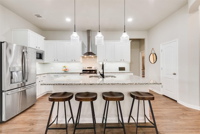 kitchen with stainless steel appliances, white cabinetry, a center island with sink, and wall chimney range hood