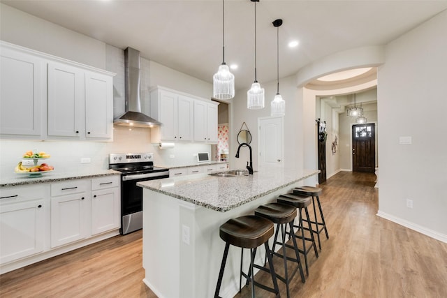 kitchen with electric stove, sink, white cabinetry, a kitchen island with sink, and wall chimney exhaust hood