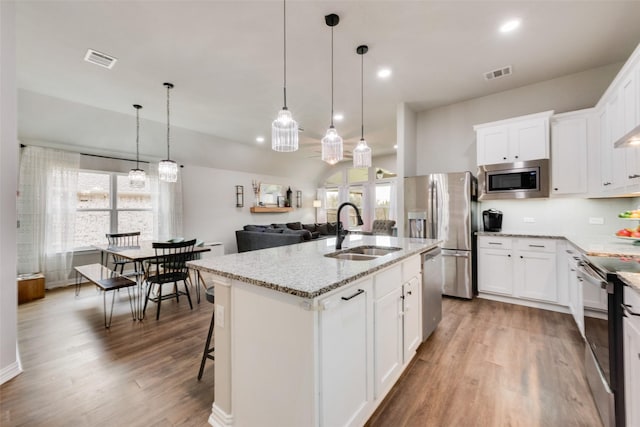 kitchen with appliances with stainless steel finishes, decorative light fixtures, white cabinetry, an island with sink, and sink