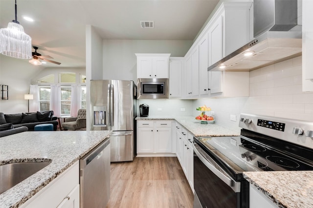 kitchen with stainless steel appliances, white cabinetry, pendant lighting, and wall chimney range hood