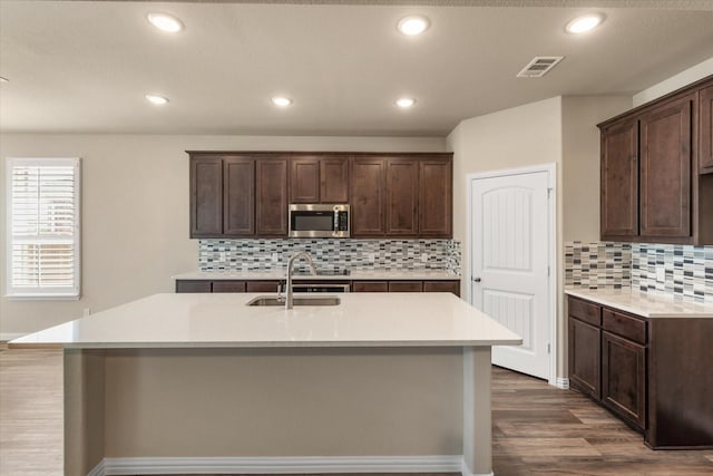 kitchen with sink, backsplash, dark hardwood / wood-style flooring, dark brown cabinetry, and a center island with sink