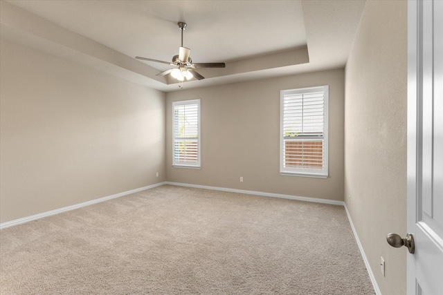 spare room featuring light colored carpet, ceiling fan, and a tray ceiling