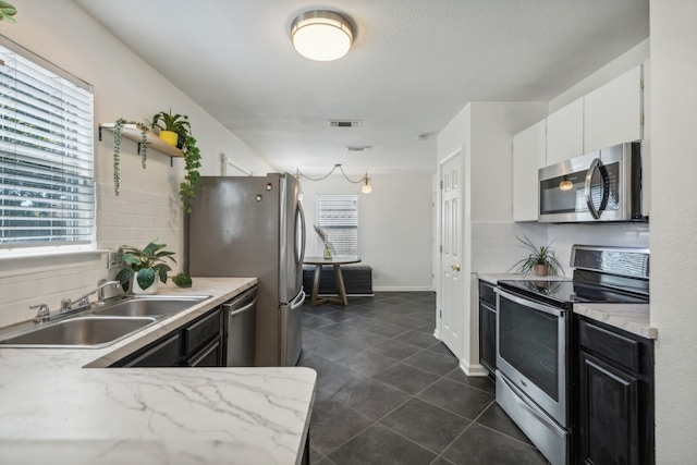 kitchen with sink, white cabinetry, tasteful backsplash, appliances with stainless steel finishes, and dark tile patterned floors