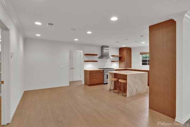 kitchen with wall chimney range hood, stainless steel stove, a kitchen breakfast bar, a kitchen island, and light wood-type flooring