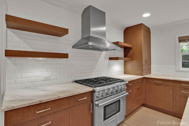 kitchen featuring wall chimney range hood, stainless steel stove, crown molding, light stone counters, and decorative backsplash