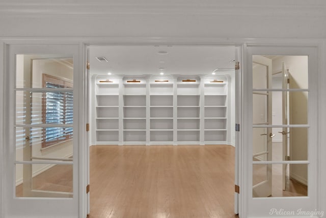 interior space featuring wood-type flooring, crown molding, and built in shelves