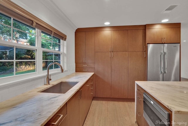 kitchen featuring sink, high end refrigerator, light stone counters, light hardwood / wood-style floors, and crown molding