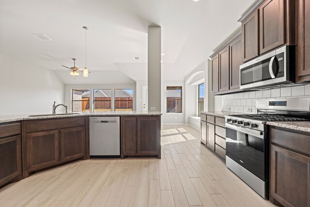 kitchen with stainless steel appliances, tasteful backsplash, dark brown cabinets, and light stone counters