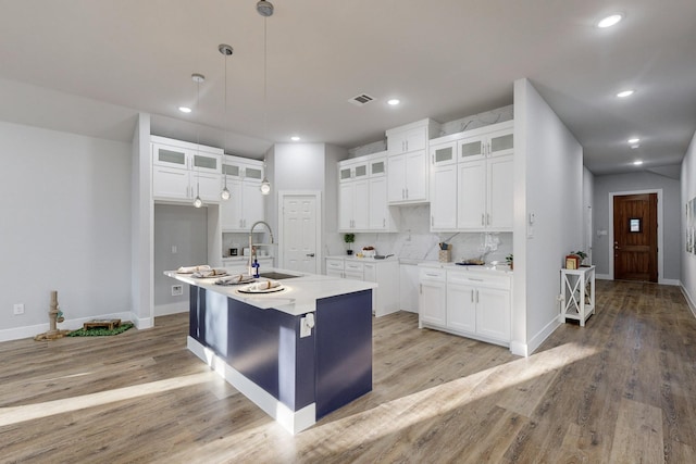 kitchen featuring an island with sink, sink, white cabinets, decorative backsplash, and light wood-type flooring