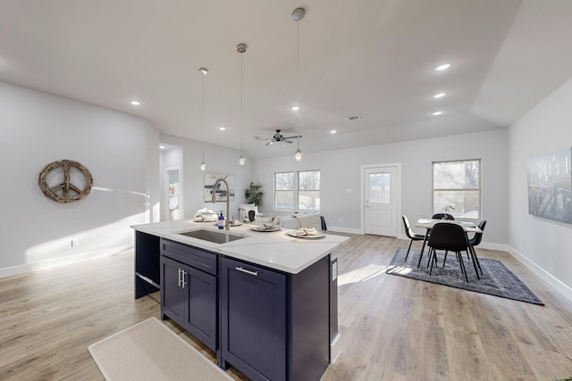 kitchen with sink, a kitchen island with sink, hanging light fixtures, light hardwood / wood-style floors, and vaulted ceiling