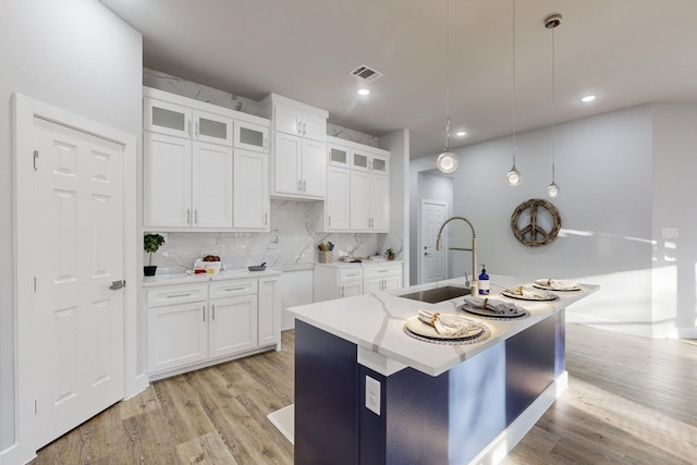 kitchen with pendant lighting, sink, white cabinets, a center island with sink, and decorative backsplash