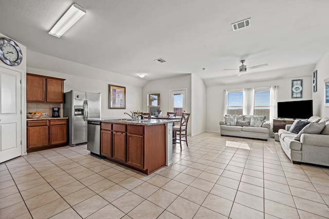 kitchen with sink, a center island with sink, light tile patterned floors, stainless steel appliances, and backsplash