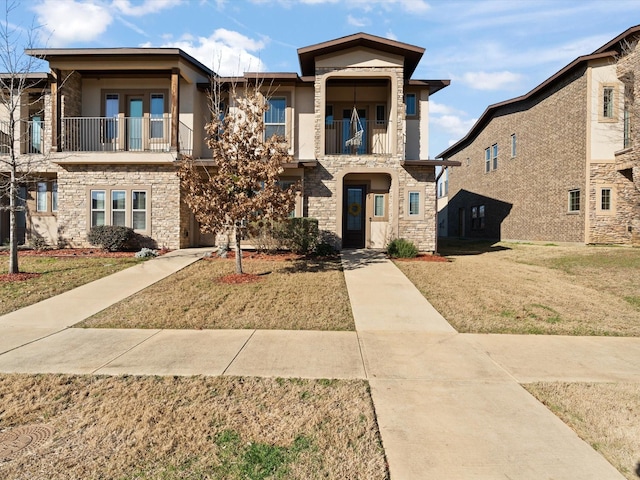 view of front of home with a balcony, stone siding, and a front yard