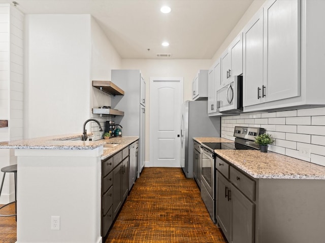 kitchen featuring visible vents, a breakfast bar, a peninsula, stainless steel appliances, and a sink