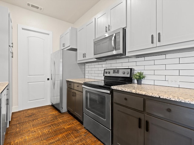 kitchen with appliances with stainless steel finishes, white cabinets, visible vents, and light stone counters