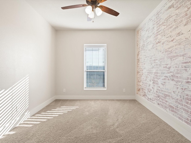 carpeted empty room featuring a ceiling fan, baseboards, and brick wall