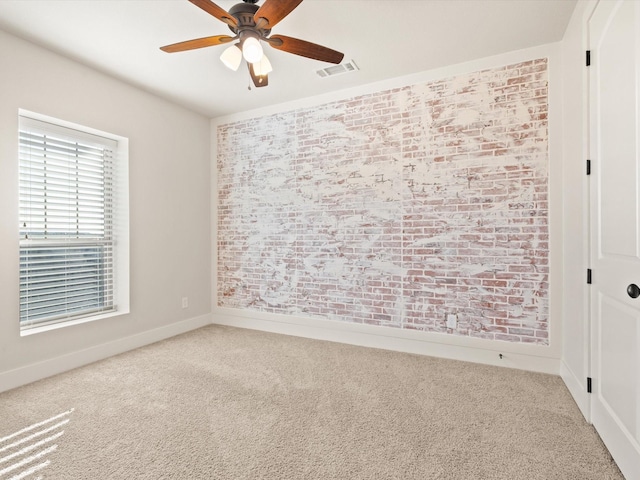 carpeted spare room with ceiling fan, brick wall, visible vents, and baseboards