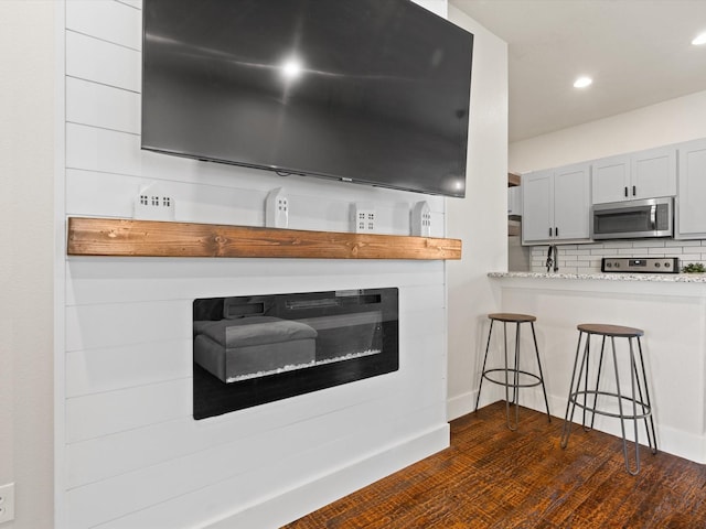 room details featuring stainless steel microwave, stove, wood finished floors, backsplash, and recessed lighting