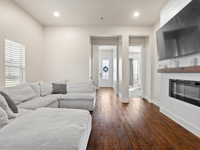 living area featuring recessed lighting, a glass covered fireplace, dark wood finished floors, and baseboards