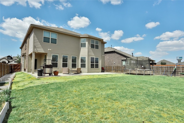 rear view of property featuring a trampoline, a patio area, and a lawn