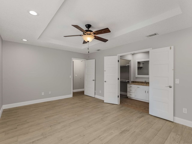 unfurnished bedroom featuring sink, a textured ceiling, light wood-type flooring, and a tray ceiling