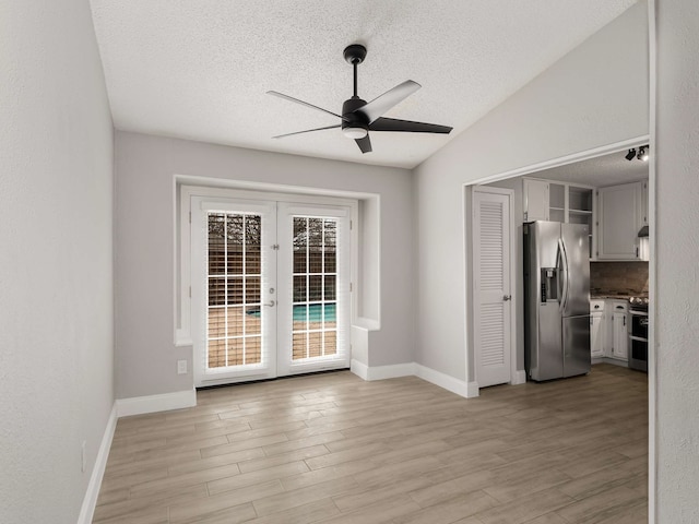 interior space featuring lofted ceiling, light hardwood / wood-style floors, french doors, and a textured ceiling