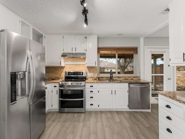 kitchen featuring sink, white cabinetry, stainless steel appliances, light stone countertops, and backsplash