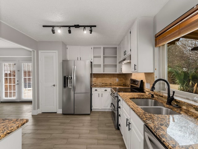 kitchen with appliances with stainless steel finishes, sink, dark stone countertops, white cabinets, and backsplash