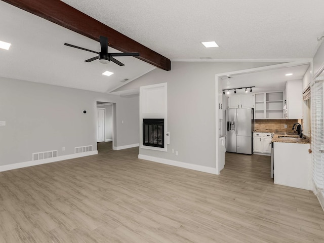 unfurnished living room with sink, vaulted ceiling with beams, light hardwood / wood-style floors, and ceiling fan