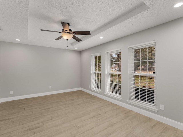 spare room with ceiling fan, a textured ceiling, light wood-type flooring, and a tray ceiling