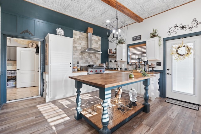 kitchen featuring pendant lighting, wall chimney range hood, white cabinetry, light hardwood / wood-style floors, and wood counters