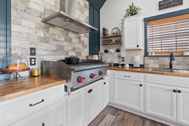 kitchen with wood counters, wall chimney range hood, sink, and white cabinets