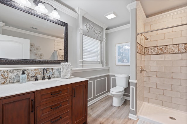 bathroom featuring crown molding, hardwood / wood-style flooring, tiled shower, vanity, and toilet