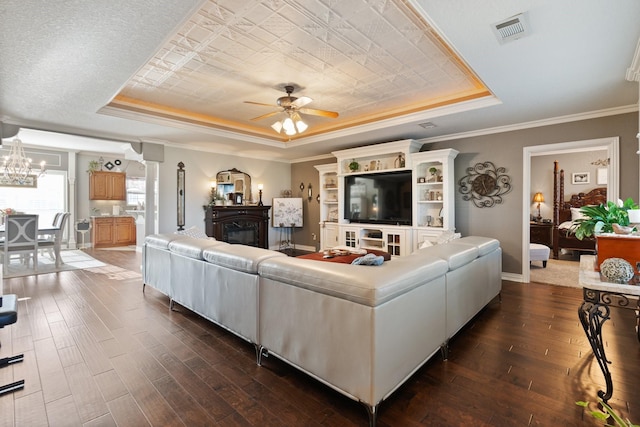 living room featuring crown molding, a tray ceiling, dark wood-type flooring, and ceiling fan with notable chandelier