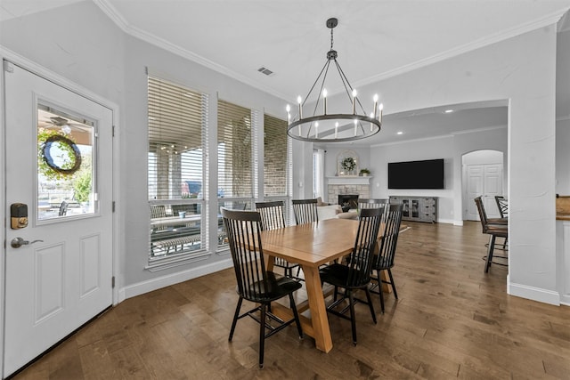 dining room with ornamental molding, arched walkways, a stone fireplace, and wood finished floors